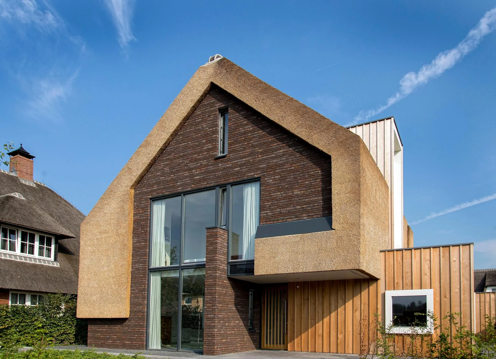 Moderne hus med stråtækt gavl og facade, murværk og træbeklædning